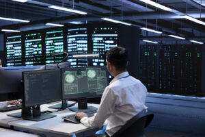 Network engineer reviewing performance dashboards in a data center with server racks in the background.