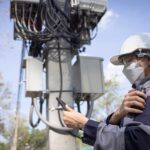 5G network engineer reviewing wireless infrastructure near a telecom tower