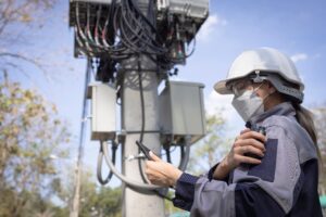 5G network engineer reviewing wireless infrastructure near a telecom tower