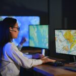 OSP GIS analyst reviewing a fiber network map on computer monitors
