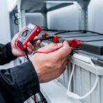 Technician testing a UPS battery string with a digital multimeter in a battery room