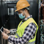 Data center facilities engineer checking high-density server racks with a tablet in a live data hall