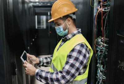 Data center facilities engineer checking high-density server racks with a tablet in a live data hall