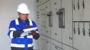 Safety manager in a hard hat and safety vest reviewing a clipboard beside electrical switchgear at a data center construction site