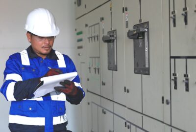 Safety manager in a hard hat and safety vest reviewing a clipboard beside electrical switchgear at a data center construction site