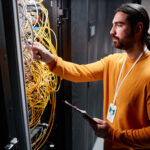 Network technician checking fiber optic patch cables in an equipment rack during a fiber capacity upgrade