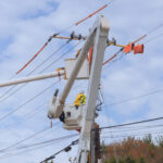 Technician in a bucket truck installing fiber on a utility pole beside existing coaxial cable during an HFC-to-fiber migration
