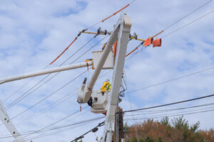 Technician in a bucket truck installing fiber on a utility pole beside existing coaxial cable during an HFC-to-fiber migration