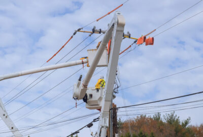 Technician in a bucket truck installing fiber on a utility pole beside existing coaxial cable during an HFC-to-fiber migration