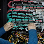 Fiber technician connecting patch cables at an optical line terminal rack during a PON upgrade