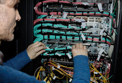 Fiber technician connecting patch cables at an optical line terminal rack during a PON upgrade